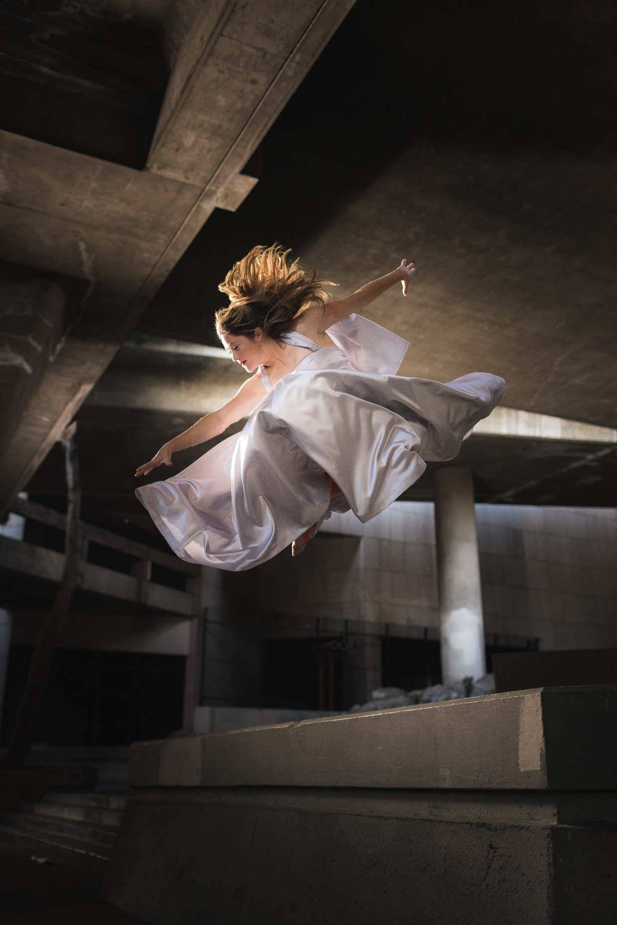 Luci Romberg freerunner parkour athlete in evening gown flying through the air under a bridge in downtown LA by andy batt