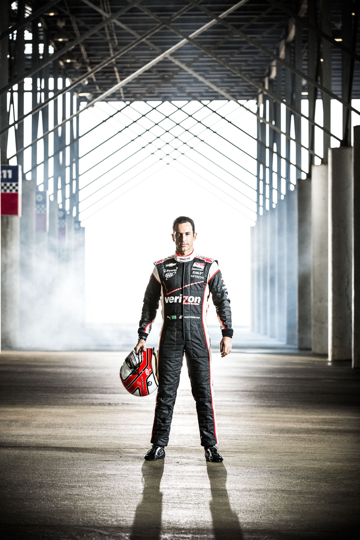 Dramatic full body portrait of athlete Helio Castroneves standing and holding helmet  IndyCar Driver Team Penske Garage Charlotte Motor Speedway below bleachers.  by Andy Batt