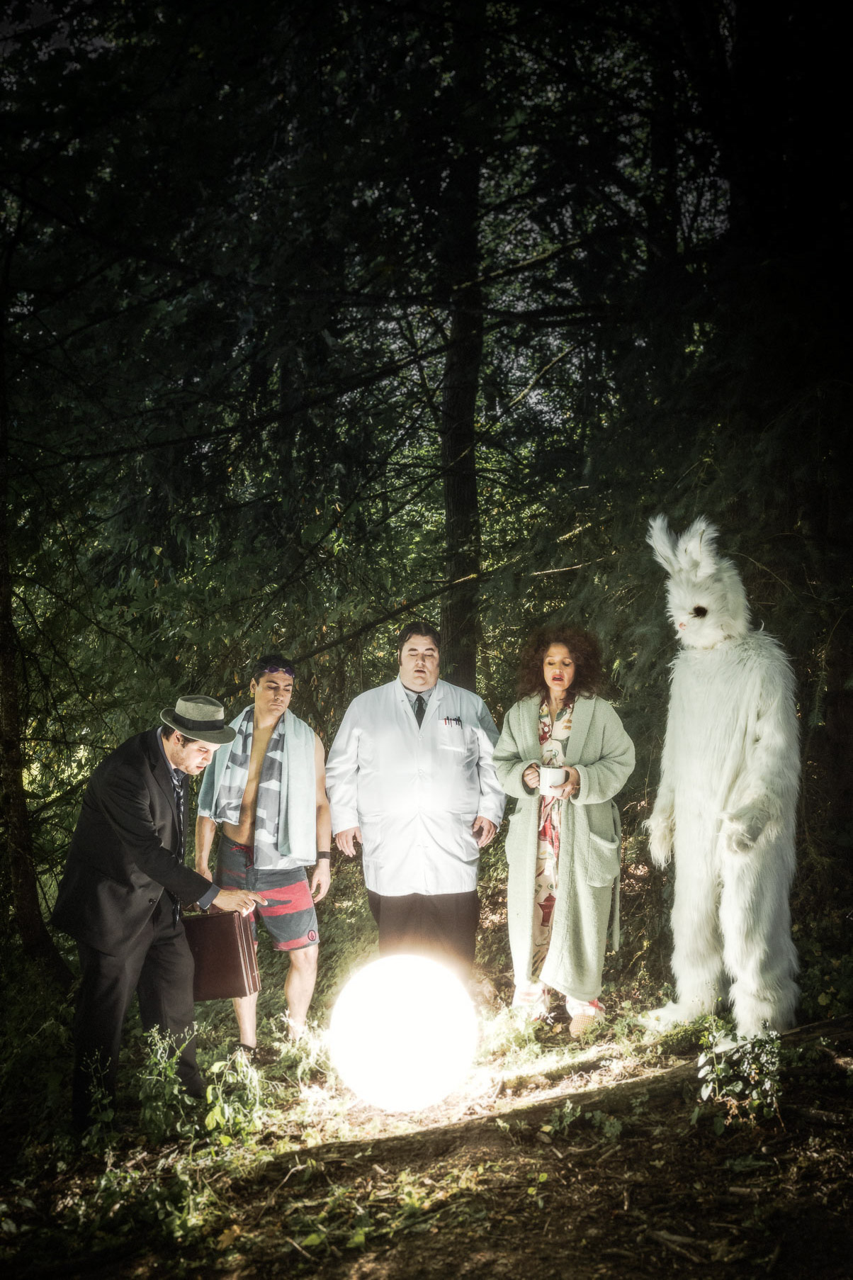 Moody scene of sketch Comedy actors Jason Rouse, Lori Ferraro, Ted Douglass, Andrew Harris and Tony St Clair in Wonderland Sketch Comedy. The performers surround a glowing white ball. The Donnie Darko rabbit is there too. Poster art by Andy Batt