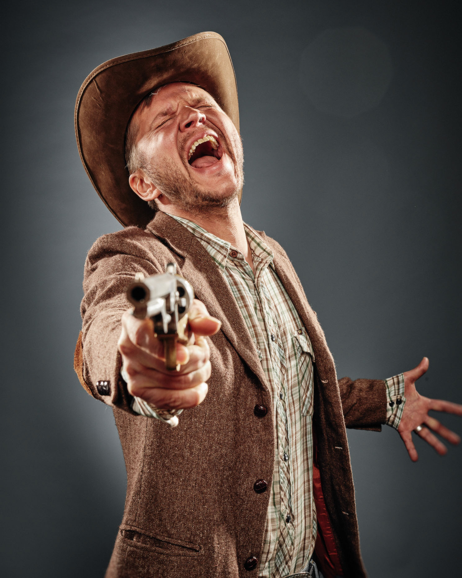 improv actor Nick Condon Curious Comedy Theater Showdown dressed as a cowboy pointing a pistol at the camera and laughing outrageously. Photo by Andy Batt