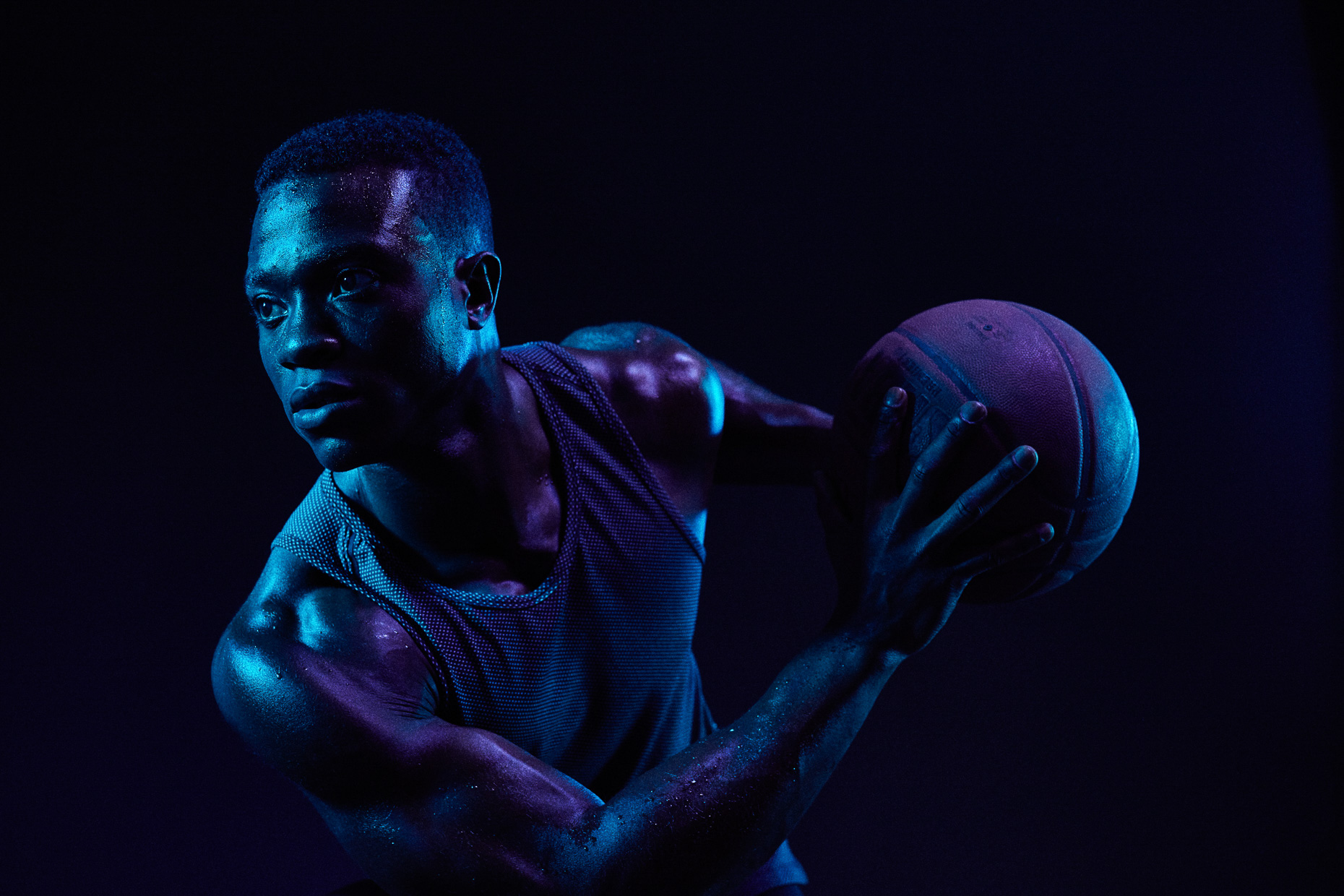Nike basketball athlete David Kojo Aidoo by Andy Batt. The player holds the ball defensively in this dark scene lit with blue gels.