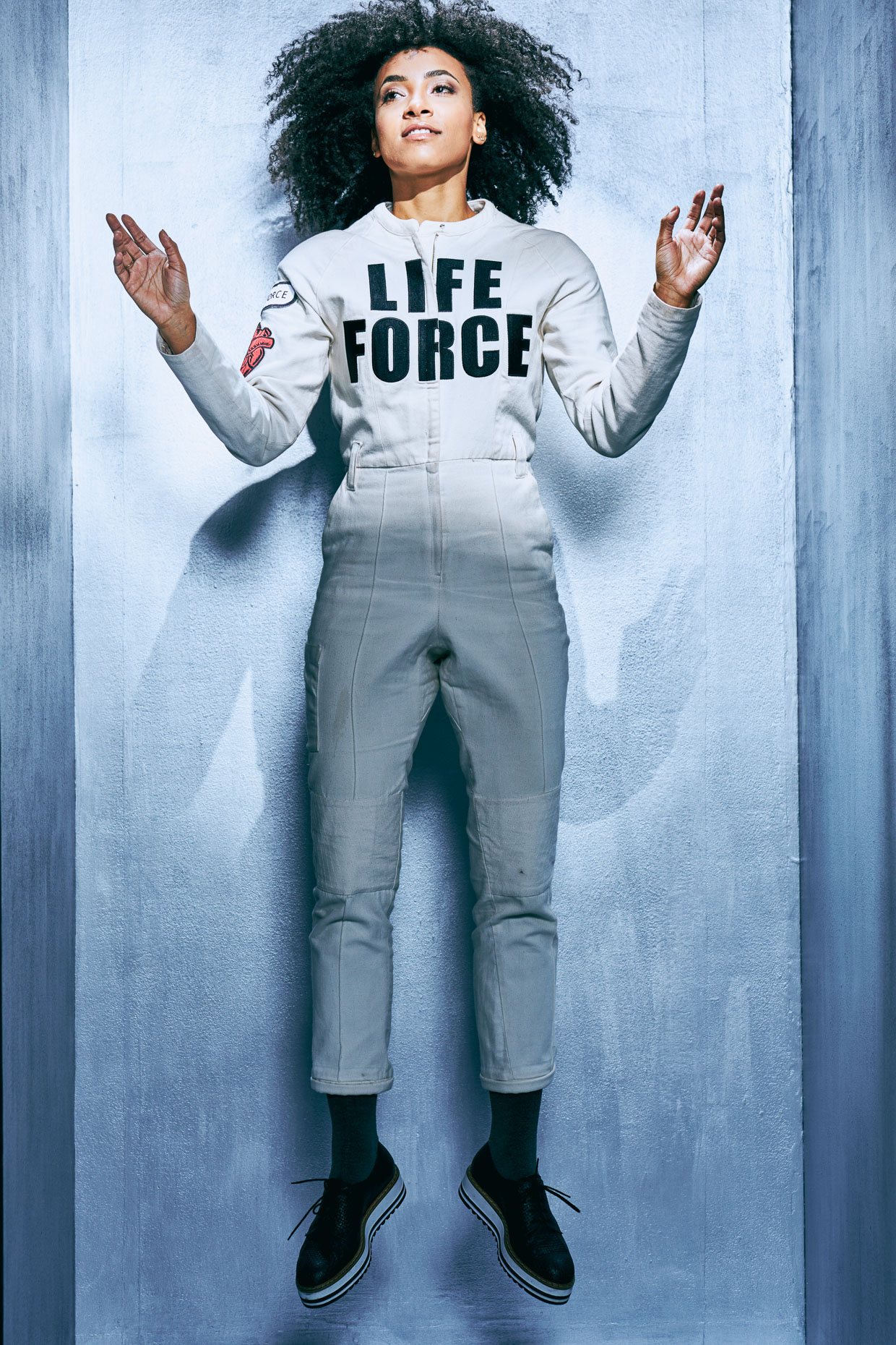 Editorial portrait of Grammy award winning jazz musician Esperanza Spalding wearing a white jumpsuit with bold black letters "LIFE FORCE" by Andy Batt