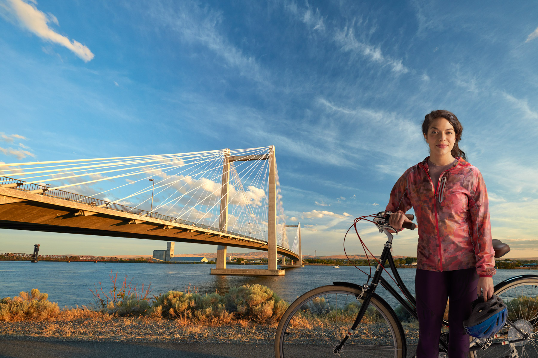 Female cyclist with bike poses in front of cable bridge in Kennewick, Washington