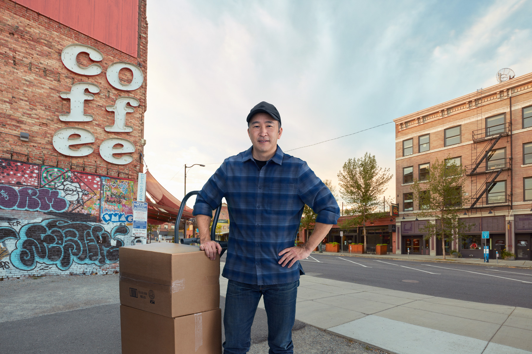 Coffee shop owner with boxes poses next to storefront in Spokane